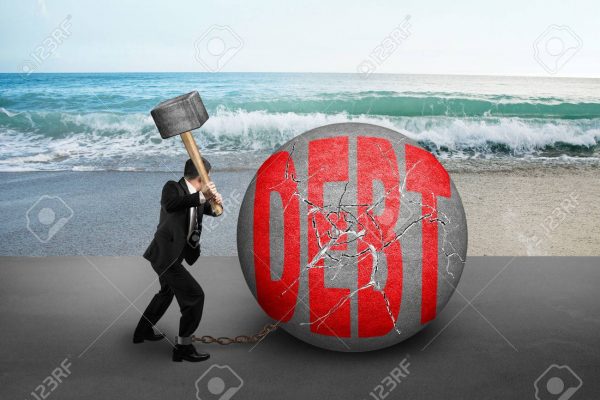 businessman holding hammer hitting cracked DEBT ball with sea beach